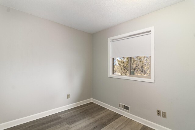 spare room with visible vents, baseboards, and dark wood-type flooring