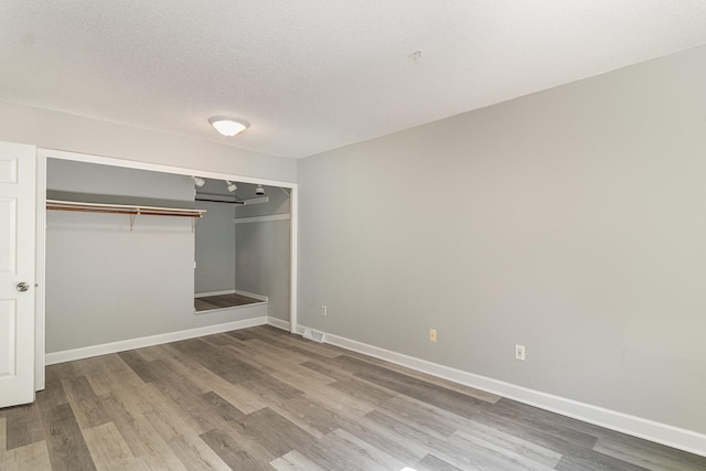 unfurnished bedroom featuring baseboards, wood finished floors, and a closet