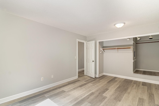 unfurnished bedroom featuring a textured ceiling, baseboards, light wood finished floors, and a closet
