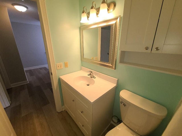 half bathroom with vanity, wood finished floors, and toilet