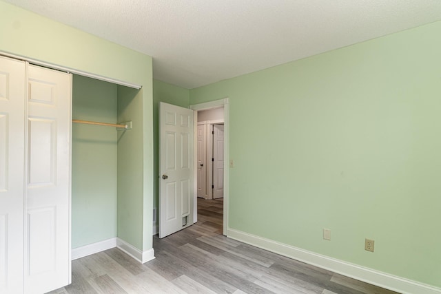 unfurnished bedroom featuring light wood-style floors, baseboards, and a closet