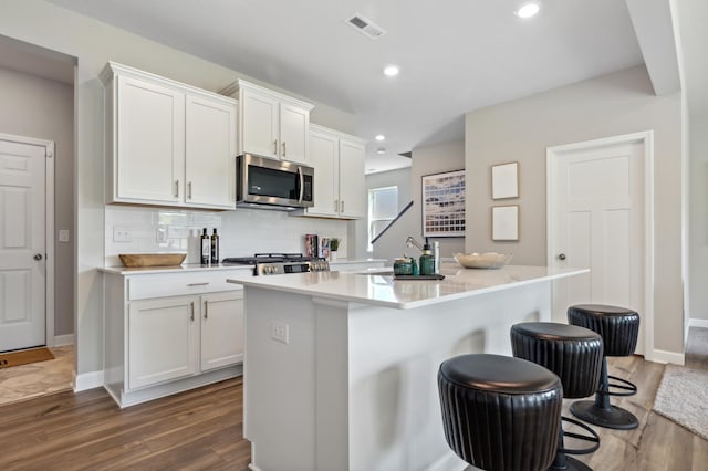 kitchen with a breakfast bar, dark hardwood / wood-style floors, an island with sink, and white cabinetry