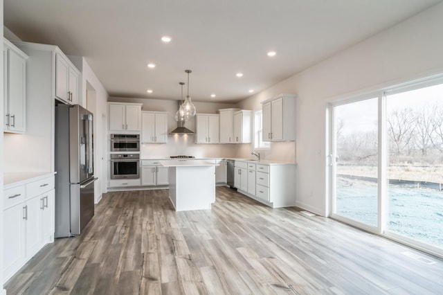 kitchen with stainless steel appliances, wall chimney exhaust hood, a kitchen island, pendant lighting, and white cabinets