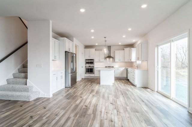 kitchen with decorative light fixtures, a center island, stainless steel appliances, white cabinets, and wall chimney exhaust hood