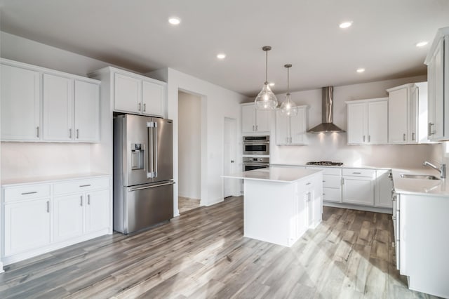 kitchen with a center island, light countertops, appliances with stainless steel finishes, a sink, and wall chimney exhaust hood