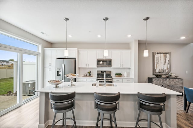 kitchen featuring hanging light fixtures, white cabinets, a kitchen island with sink, and appliances with stainless steel finishes