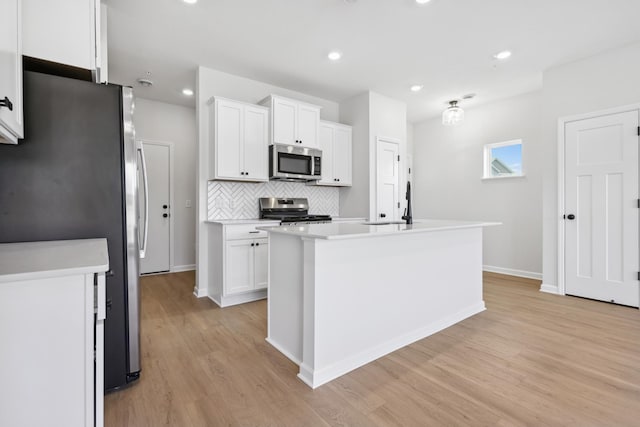 kitchen with tasteful backsplash, a kitchen island with sink, white cabinets, light wood-type flooring, and stainless steel appliances