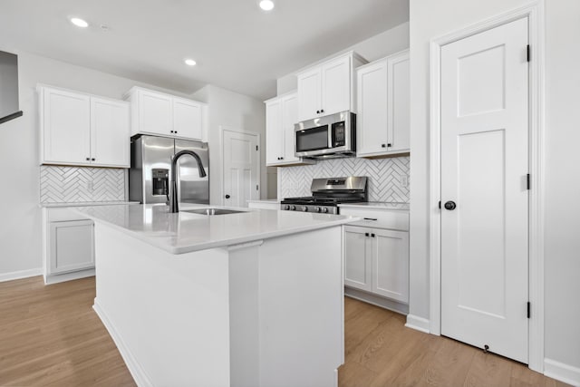 kitchen featuring appliances with stainless steel finishes, light wood-type flooring, white cabinetry, tasteful backsplash, and an island with sink