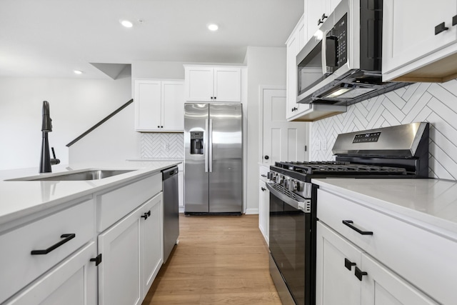 kitchen with appliances with stainless steel finishes, sink, backsplash, white cabinets, and light wood-type flooring