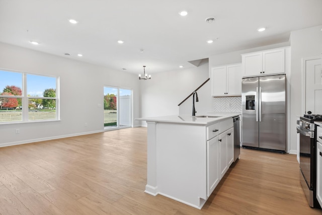 kitchen with white cabinets, light wood-type flooring, backsplash, stainless steel appliances, and a center island with sink