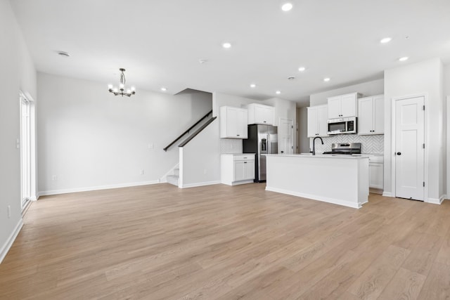 kitchen with pendant lighting, appliances with stainless steel finishes, white cabinets, a kitchen island with sink, and light hardwood / wood-style floors