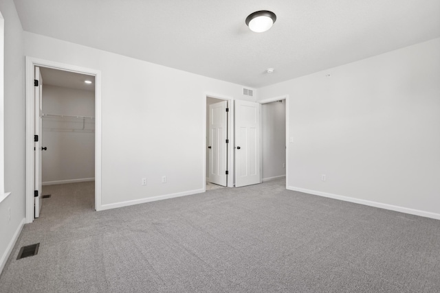 unfurnished bedroom with a spacious closet, a closet, and carpet floors