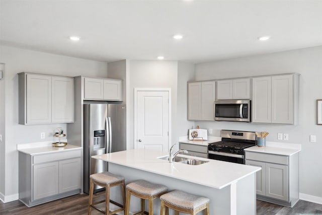 kitchen featuring gray cabinets, an island with sink, stainless steel appliances, dark hardwood / wood-style flooring, and sink