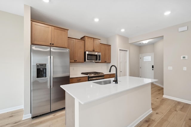 kitchen with appliances with stainless steel finishes, sink, backsplash, a kitchen island with sink, and light hardwood / wood-style floors