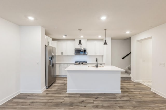 kitchen with white cabinetry, an island with sink, appliances with stainless steel finishes, decorative light fixtures, and sink