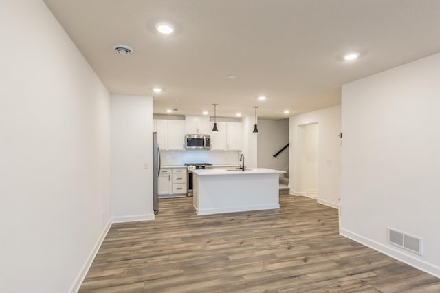 kitchen featuring hardwood / wood-style floors, pendant lighting, white cabinetry, appliances with stainless steel finishes, and an island with sink