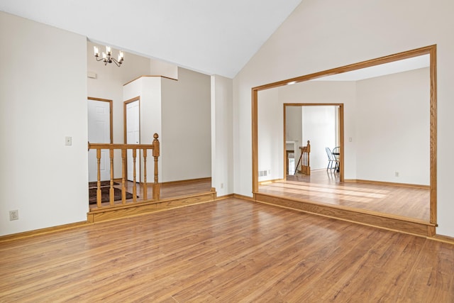 spare room featuring light wood finished floors, baseboards, visible vents, high vaulted ceiling, and a notable chandelier