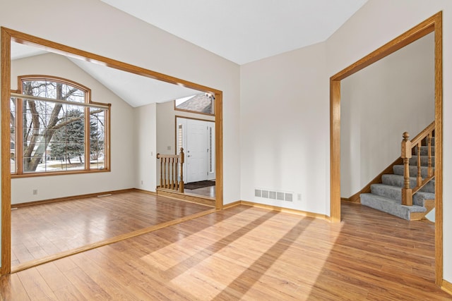 empty room featuring light wood finished floors, baseboards, visible vents, stairs, and vaulted ceiling