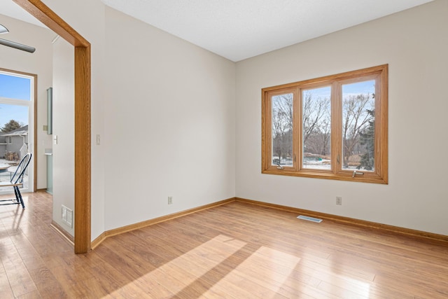 empty room with light wood finished floors, plenty of natural light, and visible vents