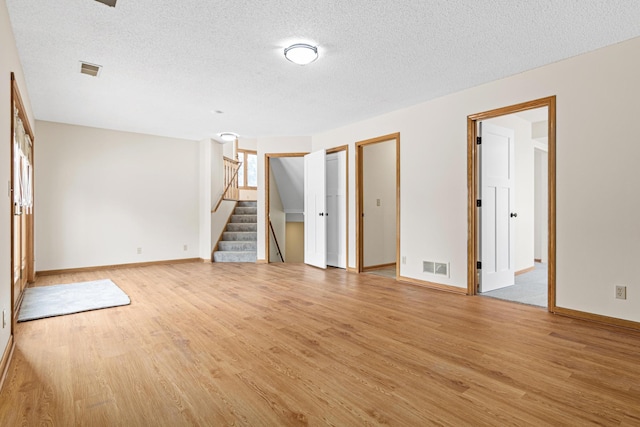 empty room featuring light wood finished floors, stairs, visible vents, and a textured ceiling