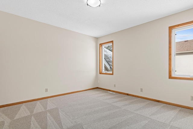 empty room with light carpet, a textured ceiling, and baseboards