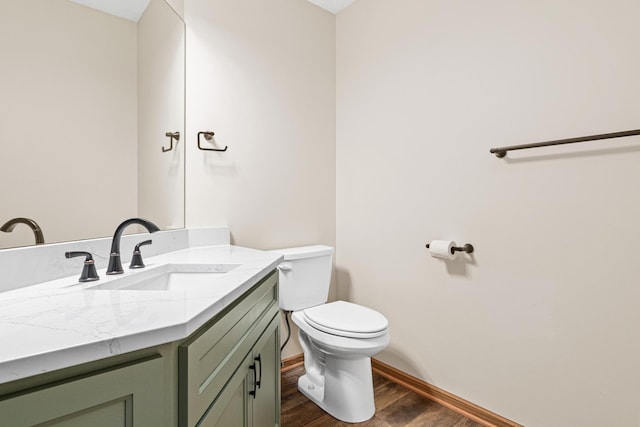 half bathroom with vanity, wood finished floors, toilet, and baseboards