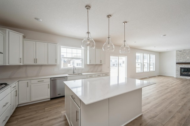 kitchen featuring dishwasher, a center island, a wealth of natural light, a fireplace, and white cabinets