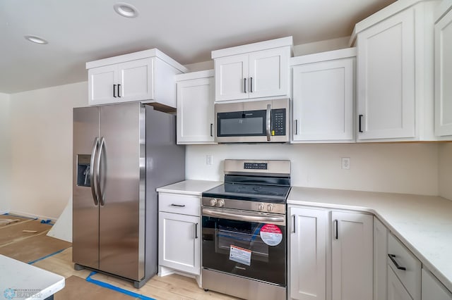 kitchen featuring stainless steel appliances, white cabinetry, light stone countertops, and light wood-type flooring