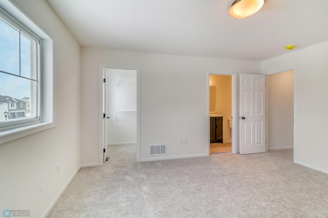 unfurnished bedroom with a walk in closet, light colored carpet, ensuite bath, and a closet