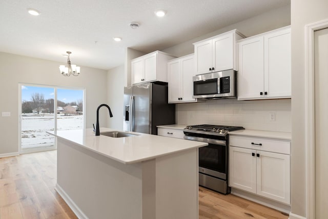 kitchen featuring appliances with stainless steel finishes, pendant lighting, white cabinetry, sink, and a kitchen island with sink