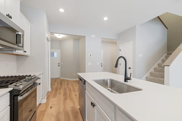 kitchen with light wood-type flooring, appliances with stainless steel finishes, sink, and white cabinets