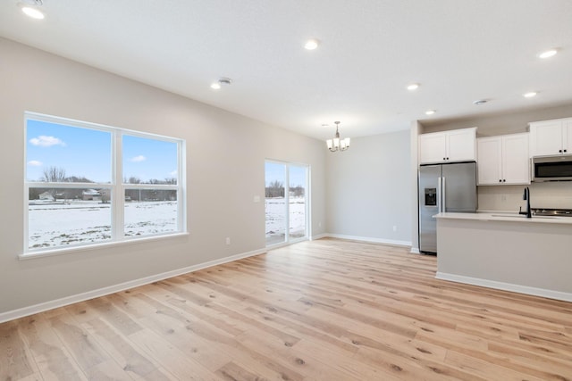 kitchen with sink, appliances with stainless steel finishes, white cabinets, decorative light fixtures, and light wood-type flooring