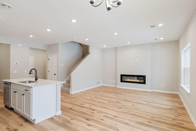 kitchen featuring sink, a center island with sink, stainless steel dishwasher, light hardwood / wood-style floors, and white cabinets