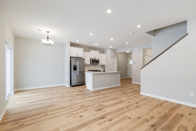 interior space with appliances with stainless steel finishes, pendant lighting, white cabinetry, a center island with sink, and light wood-type flooring