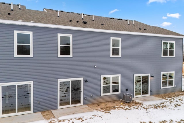 snow covered back of property featuring central AC and a patio