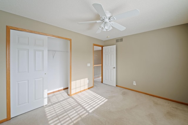 unfurnished bedroom with ceiling fan, a textured ceiling, a closet, and light carpet