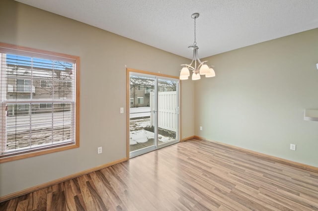 spare room featuring light hardwood / wood-style floors, a textured ceiling, and an inviting chandelier