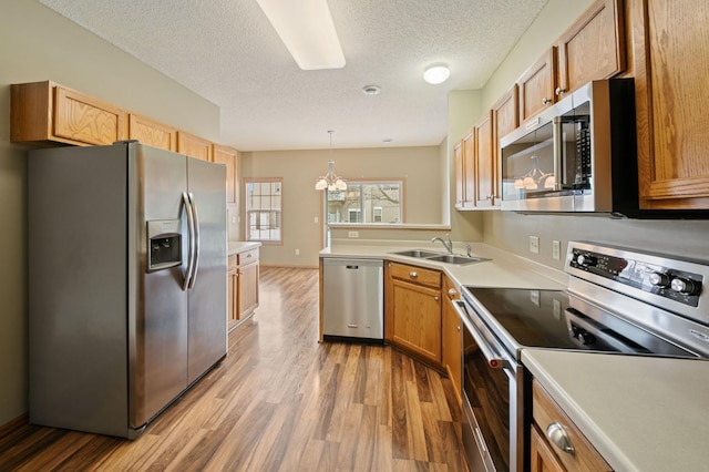 kitchen with pendant lighting, wood-type flooring, sink, a textured ceiling, and stainless steel appliances