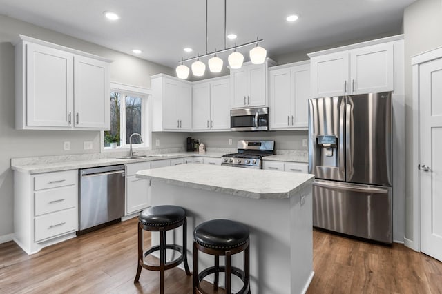 kitchen with a kitchen bar, hardwood / wood-style flooring, stainless steel appliances, a kitchen island, and white cabinets