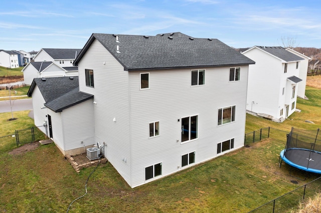 rear view of property featuring a lawn, central AC unit, and a trampoline