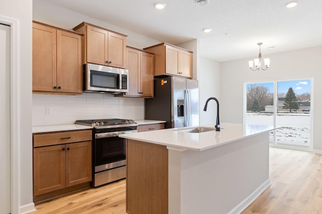 kitchen featuring sink, decorative light fixtures, a center island with sink, stainless steel appliances, and light hardwood / wood-style floors