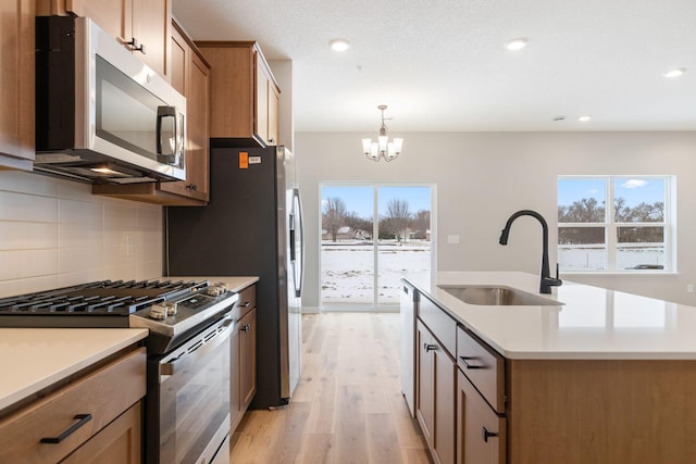 kitchen with a center island with sink, light wood finished floors, a sink, stainless steel appliances, and backsplash