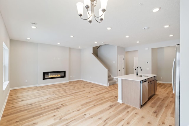 kitchen featuring an island with sink, a sink, appliances with stainless steel finishes, a glass covered fireplace, and light wood-type flooring