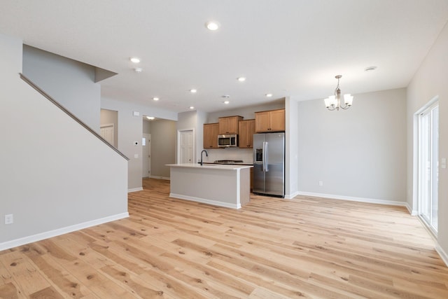 kitchen featuring a kitchen island with sink, baseboards, light wood finished floors, and stainless steel appliances