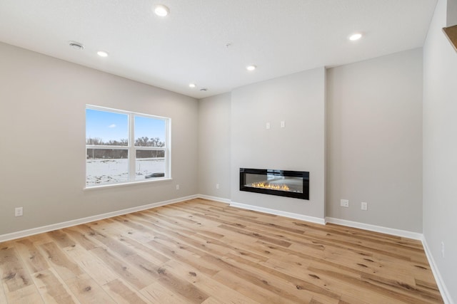 unfurnished living room with a glass covered fireplace, recessed lighting, baseboards, and light wood-style floors