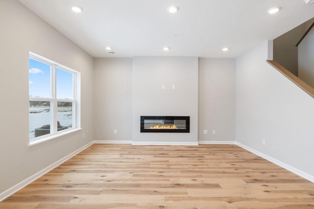 unfurnished living room with recessed lighting, a glass covered fireplace, light wood-style flooring, and baseboards