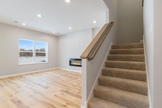 staircase with a glass covered fireplace, recessed lighting, baseboards, and wood finished floors