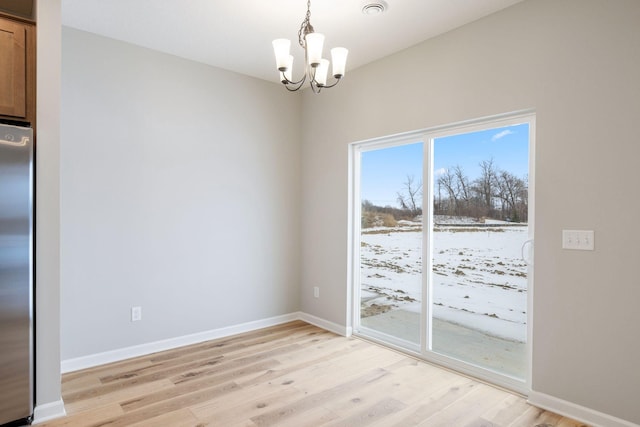 unfurnished dining area featuring light wood-style flooring, a notable chandelier, and baseboards