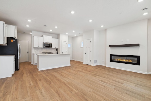 kitchen with light hardwood / wood-style flooring, white cabinetry, backsplash, stainless steel appliances, and a center island with sink