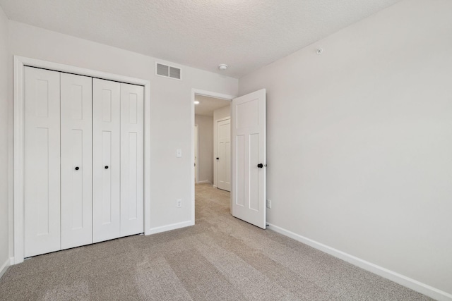 unfurnished bedroom featuring light colored carpet, a textured ceiling, and a closet